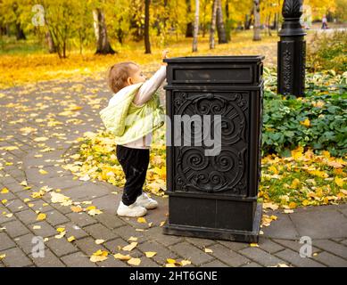 cute little baby throws trash into trash can in autumn park. instilling cultural norms from birth Stock Photo