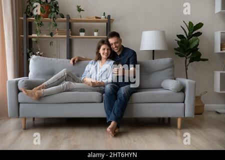 Relaxed happy young family couple using smartphone. Stock Photo