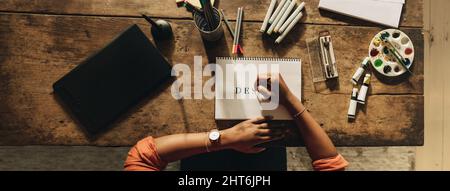Woman drawing the word ''DESIGN'' while sitting at her creative workstation. High angle view of a female graphic designer working on a new project. An Stock Photo
