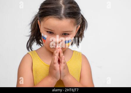 Sad child with Ukrainian and Russian hearts prays on a gray background Stock Photo