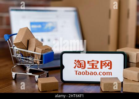 Taobao is a Chinese online shopping platform. Smartphone with Taobao logo on the screen, shopping cart and laptop. Stock Photo