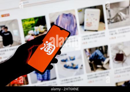 Taobao is a Chinese online shopping platform. A smartphone with the Taobao logo in a hand on background of the catalog from the site. Stock Photo