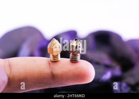 3D printer nozzles with new and used conditions held in the tip of a finger Stock Photo