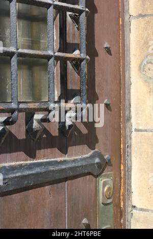 An old medieval door fortified with a metal grating as a protective covering over the window. Stock Photo