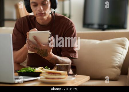 Creative young man listening to music in headphones and writing song in notepad Stock Photo