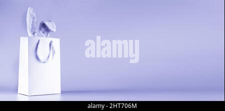 Wide banner on a very peri lavender background. The concept of online shopping for Easter, purchases and sale for the holiday. Gift bag with bunny Stock Photo
