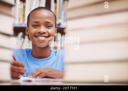 He loves hitting the books. An african american boy surrounded by books at the library. Stock Photo