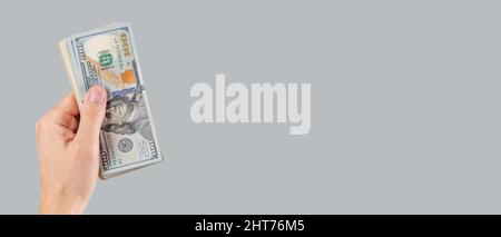 Banner with hand giving US one hundred dollar bills stack on grey background. Salary, loan. Copyspace. High quality photo Stock Photo