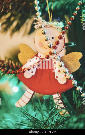 A vertical closeup of a wooden angel ornament hanging from a Christmas tree on a blurry background Stock Photo