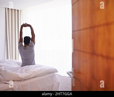 Best nights sleep ever. A young man stretching out after waking. Stock Photo