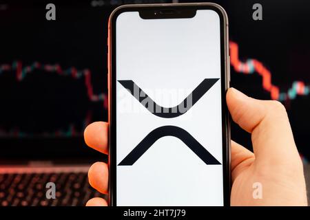 XRP cryptocurrency logo on the screen of smartphone in mans hand with downtrend on the chart on a red light background, February 2022, San Francisco, USA. Stock Photo