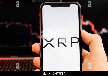 XRP cryptocurrency logo on the screen of smartphone in mans hand with downtrend on the chart on a red light background, February 2022, San Francisco, USA. Stock Photo