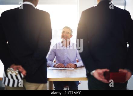 Office surprise. Rearview shot of a two employees holding surprise gifts for their boss. Stock Photo