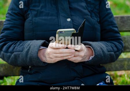 Casually dressed woman sitting on park bench using  mobile cell  phone selective focus Stock Photo