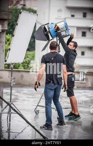 Behind the scene. Filmmaking lighting technician electric engineer adjusting and setup lights for movie film scene. Light Department. Film Crew Stock Photo