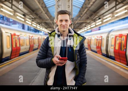 man standing on a platform looking at his phone waiting for a train Stock Photo