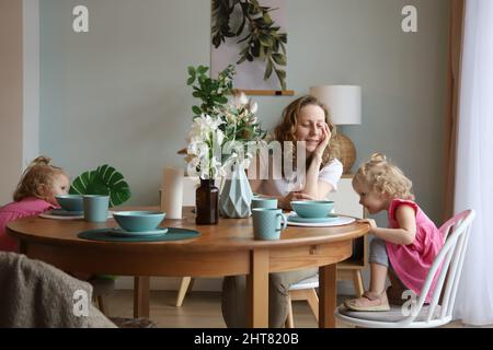 Mom and twin girls are sitting at the dinner table. Stock Photo