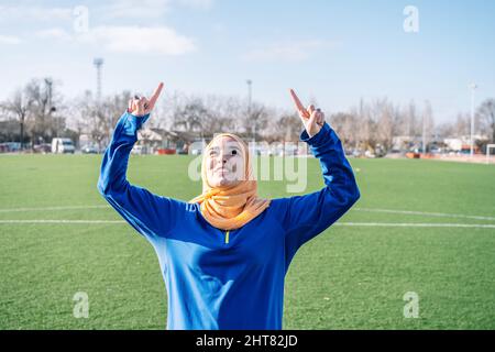 Smiling Arab female raising forefingers on sports field Stock Photo
