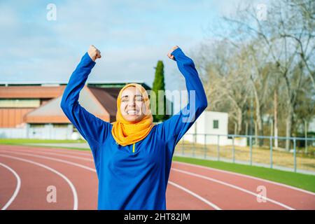 Joyful ethnic woman raising hands up and celebrating sport achievement Stock Photo