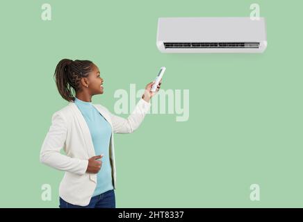 Woman using remote control turns on or adjusts air conditioner isolated on light green background. Stock Photo
