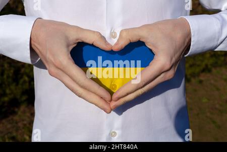 man holidng his hands in heart shaped on white shirt with ukraine flag colors support concept . Stock Photo