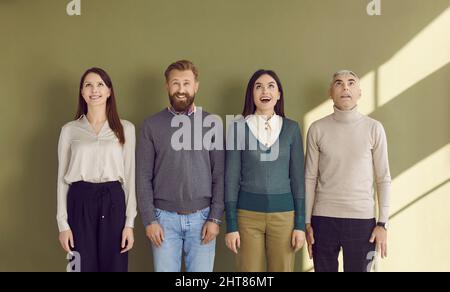 Portrait of smiling four surprised and amazed business people standing in row and looking up. Stock Photo