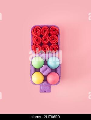 Creative concept of box of colorful Easter eggs on the one side and full of red roses on the other. Pastel color flat lay on spring pink background. Stock Photo