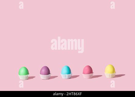 Easter decoration with pastel colored eggs that looks like tasty  cookies. Colorful concept of cupcakes on pink background with copy space. Stock Photo