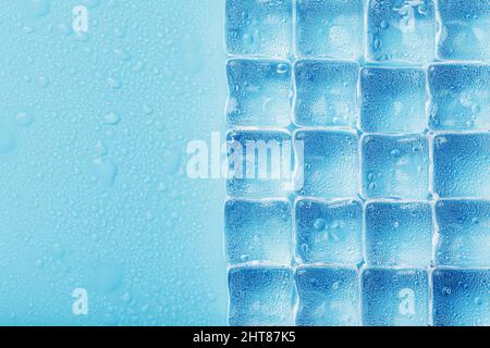 Ice cubes are scattered with water drops scattered on a blue background. Close up. Refreshing ice. Stock Photo