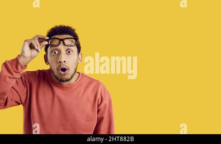 Portrait of funny surprised young man looking at you with shocked expression on yellow background. Stock Photo