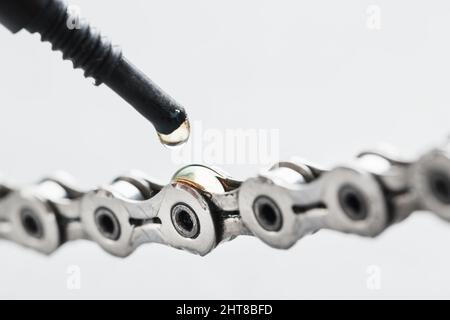 Greasing a bicycle chain with a drop of golden oil close-up on a gray background. Taking care of the bike drive system. Stock Photo