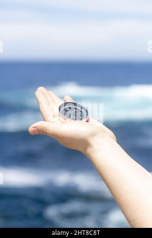 A closeup of a hand holding a compass in front of the ocean. Travel, concepts Stock Photo