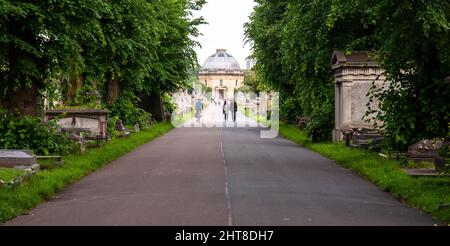 London, England, UK - June 18, 2013: Pedestrians and a cyclist pass graves and tombstones on a path through Brompton Cemetery in Chelsea, London. Stock Photo