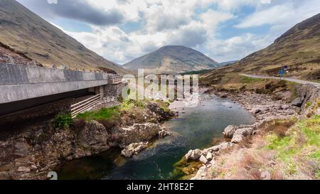 The River Coe tumbles over rocks beside the A82 road in Glen Coe valley under the mountains of the Highlands of Scotland. Stock Photo
