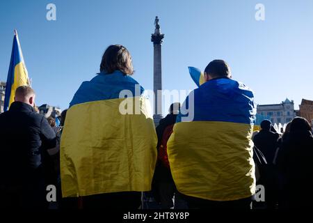 Two men wearing Ukraine flags, protest against Russia's invasion of Ukraine, Trafalgar Square, Nelson's column, London, UK, 27 February 2022 Stock Photo