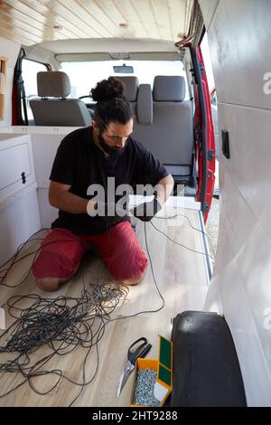 Hispanic male working on electrical equipment inside a camper van Stock Photo