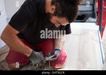 Hispanic male cutting cable for electrical equipment inside a camper van Stock Photo