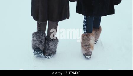 Two girls in fur coats and fur boots walk in the cold winter on the white snow Stock Photo