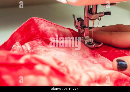 closeup of sewing machine needle sewing a red fabric with red thread with copy space, detail of female hands holding a red fabric that is sewing in he Stock Photo
