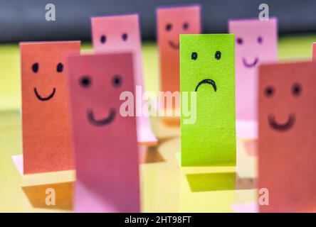 Sad face on a green sticker surrounded with smiley faces on pink stickers Stock Photo