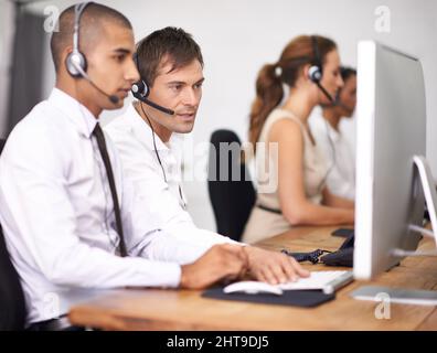 Have you turned it off and back on again. Shot of a group of help desk operators wearing headsets and working in an office. Stock Photo