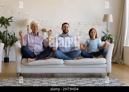 Multi generational men meditating together seated cross-legged on couch Stock Photo