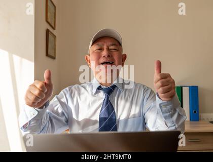 A senior executive in the office giving the thumbs up sign with a big smile after closing a big deal on line. Stock Photo