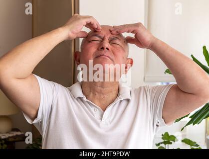 A matured senior man at home pinching and rubbing his head feeling unwell and or in pain. Feeling unwell concept. Stock Photo