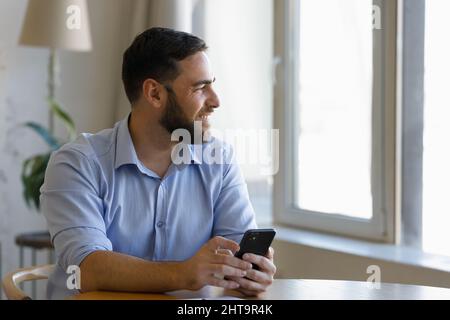 Handsome millennial man sit at table with cellphone in hands Stock Photo