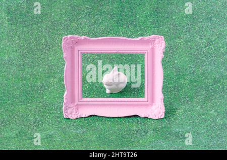 A white ceramic bunny on grass background in a stylish pastel pink frame. Creative concept for easter celebration card or banner. Surreal spring festi Stock Photo