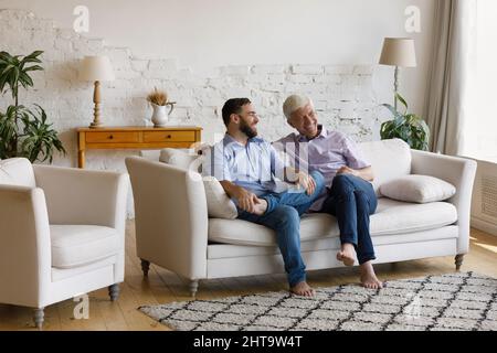 Cheerful man his senior father talking sit on sofa Stock Photo