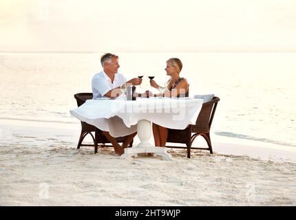 Middle aged couple enjoying romantic dinner at the beach. Shot of a mature couple enjoying a romantic dinner on the beach. Stock Photo