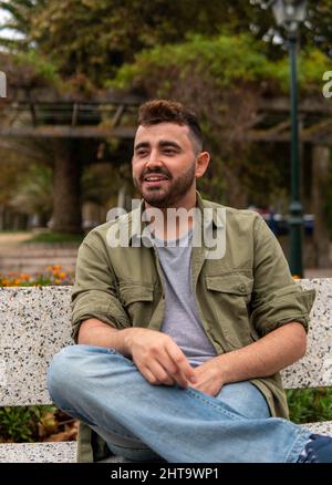 A bearded Caucasian man wearing jacket sitting on a bench in Vigo, Spain Stock Photo