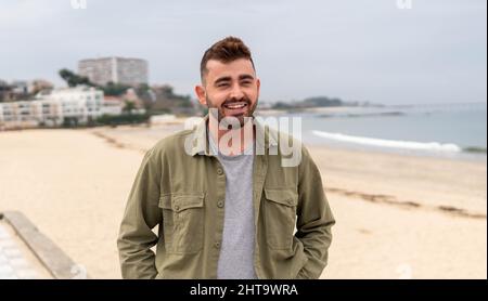 Smiling bearded Caucasian man wearing jacket on the beach in Vigo, Spain Stock Photo